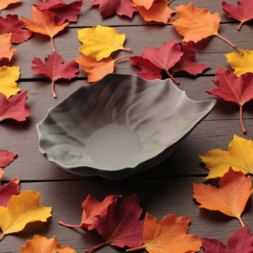 Decorative leaf-shaped bowl on a wooden surface with autumn leaves