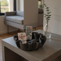 Decorative bowl with remotes and a card on a table in a living room.