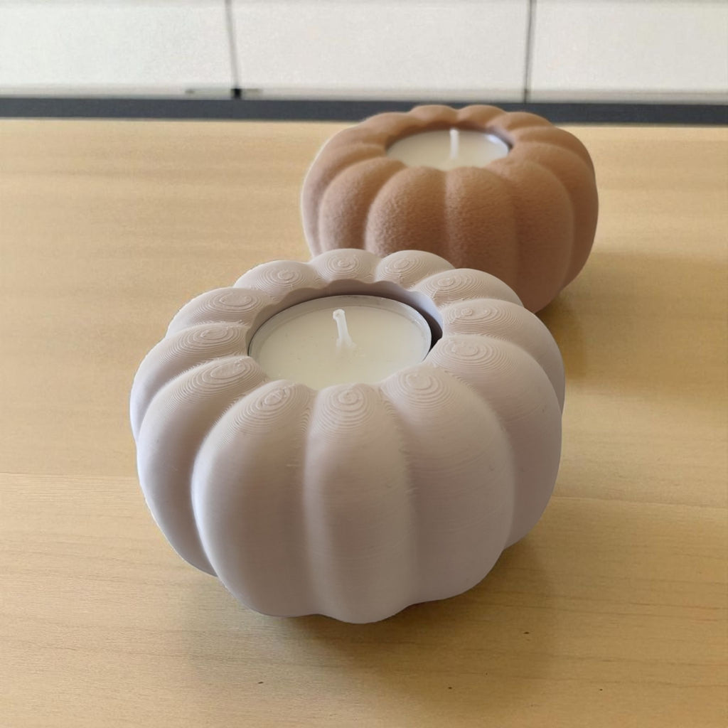 Two pumpkin-shaped candle holders with candles inside on a wooden surface.