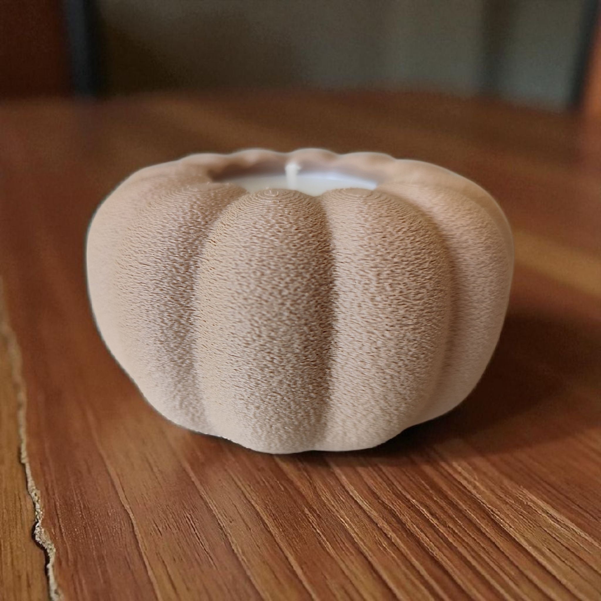 Textured beige pumpkin-shaped candle on a wooden surface
