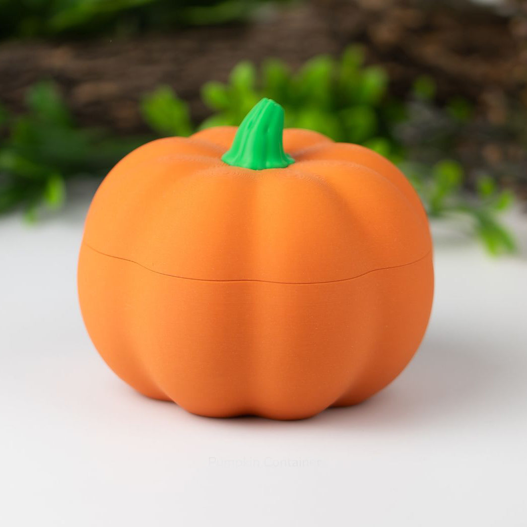 Pumpkin-shaped container with a green stem on a white surface with blurred greenery in the background