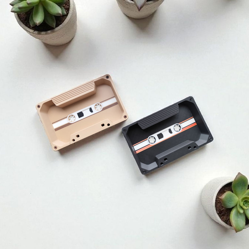 Two cassette tapes on a white surface with small potted plants around.