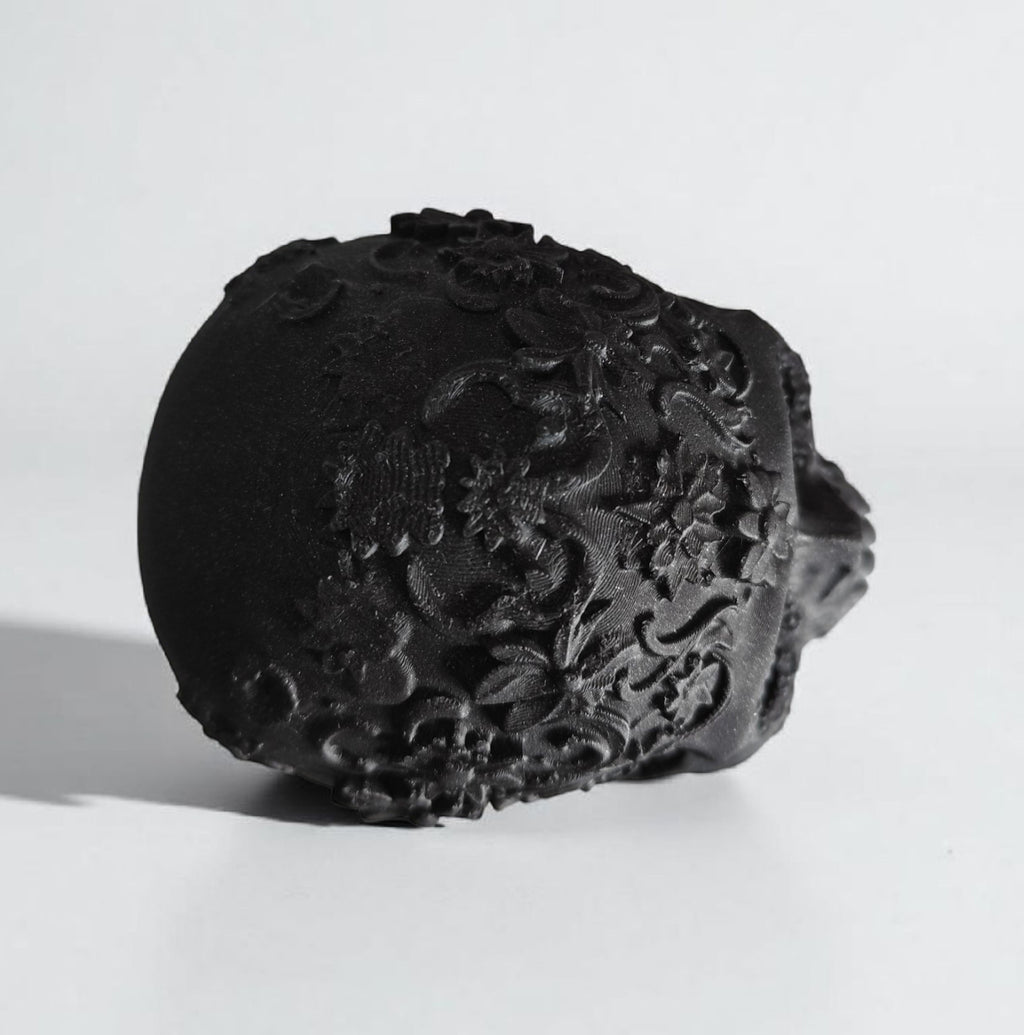 Black decorative skull with intricate carvings on a white background