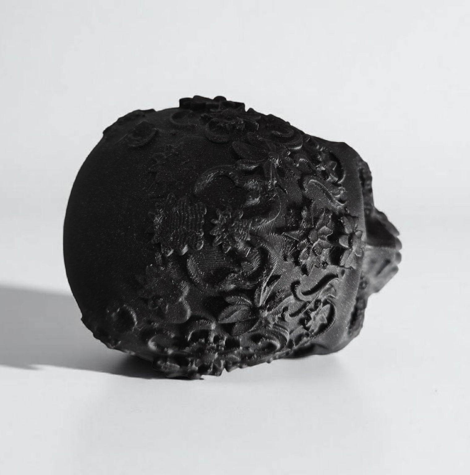Black decorative skull with intricate carvings on a white background