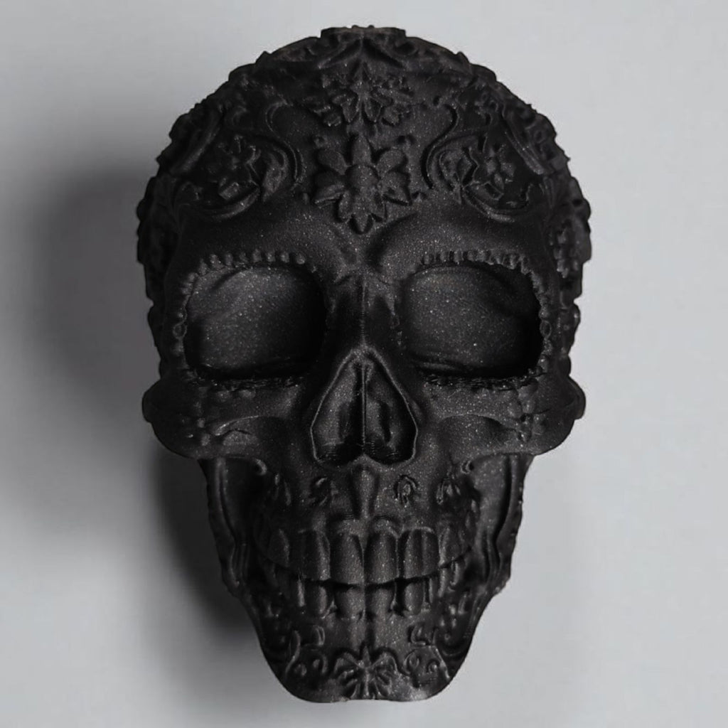 Black skull-shaped decorative item with intricate designs on a gray background