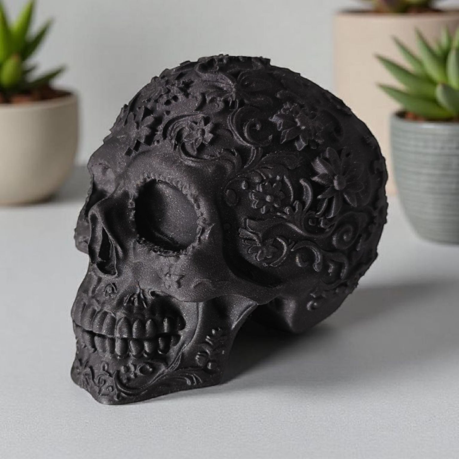 Decorative black skull with floral patterns on a light surface, with plants in the background.
