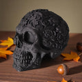 Decorative black skull with floral patterns on a wooden surface with autumn leaves and acorns.