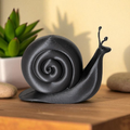 Black snail sculpture on a wooden surface with a plant in the background