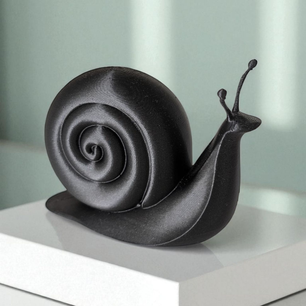 Black snail sculpture on a white surface with a light green background