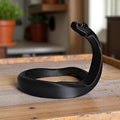 Minimalist black mamba snake sculpture on a modern wooden bookshelf.