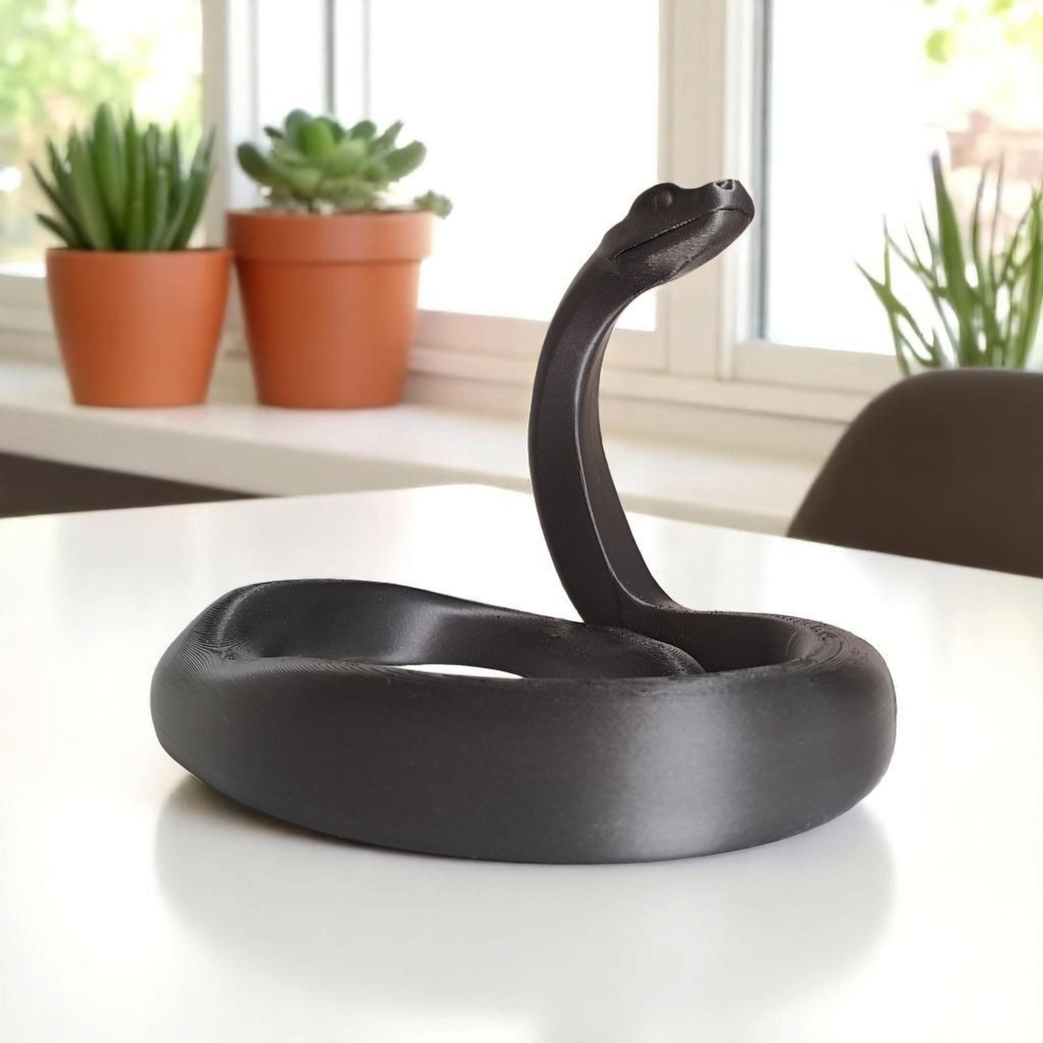 The black mamba sculpture on a clean office desk next to a plant.