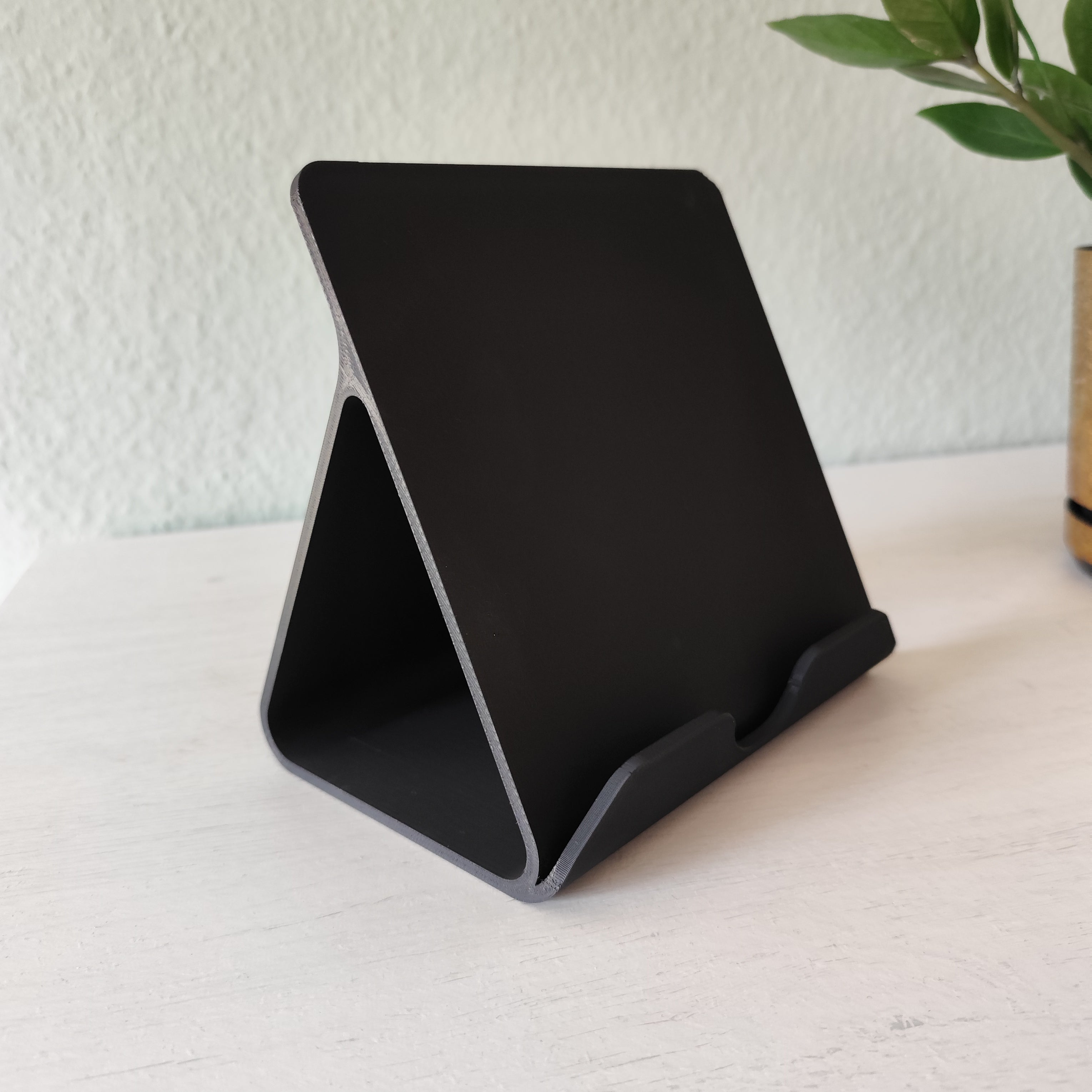 Black phone stand on a white surface with a light gray textured wall in the background