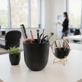 Black holder with makeup brushes and a comb on a desk in an office setting.