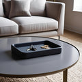 Round coffee table with a dark tray holding keys and coins, in front of a light gray sofa.