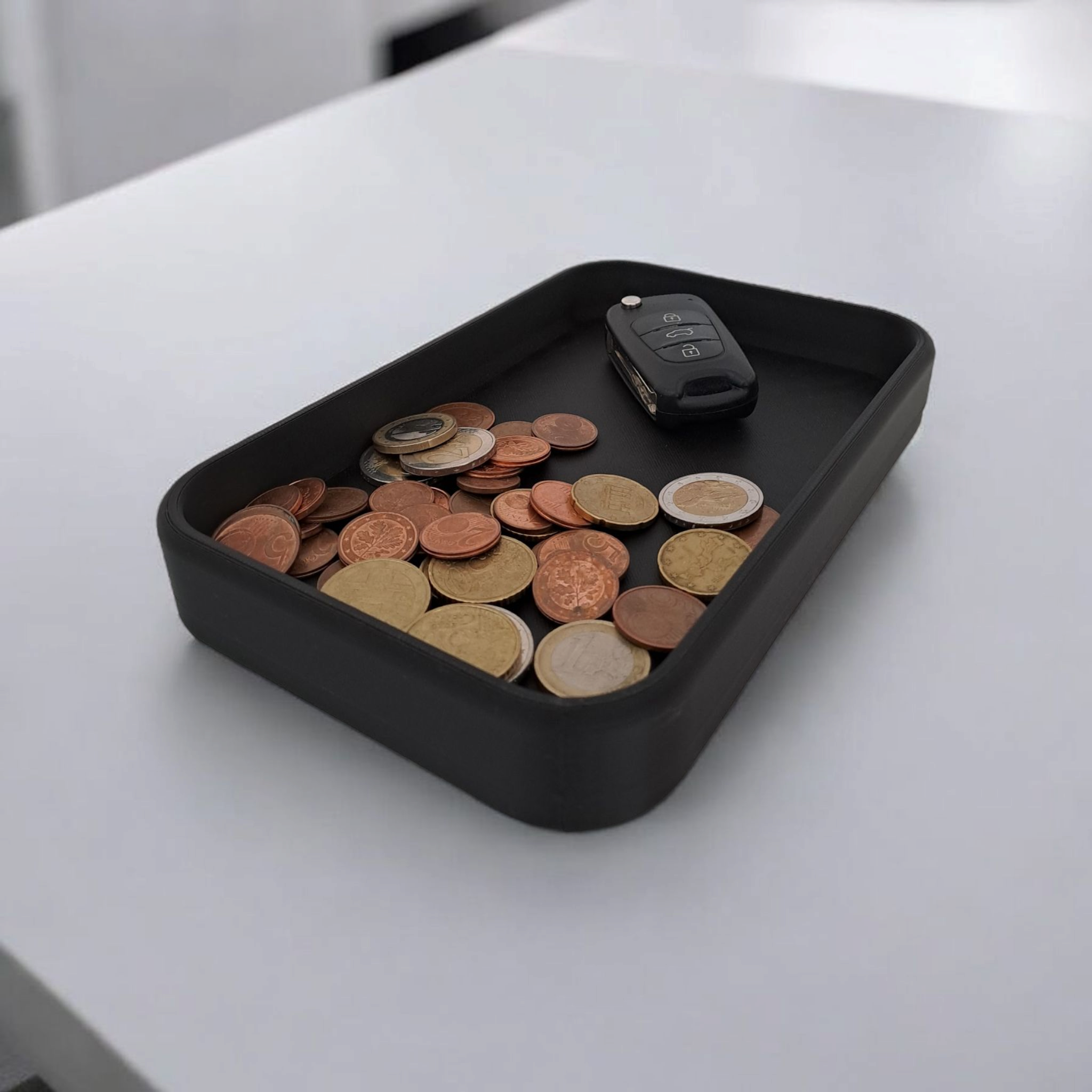 Black tray with coins and a car key on a white surface