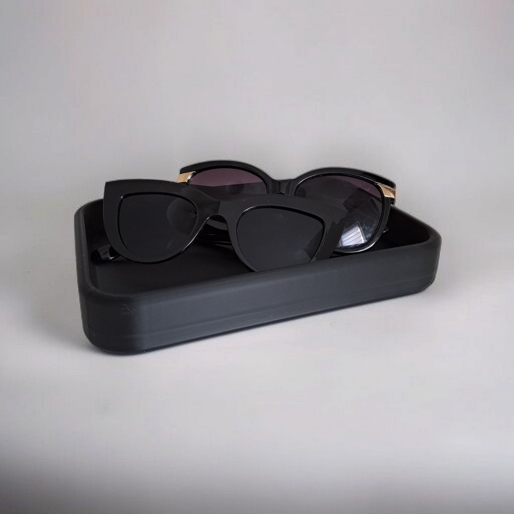 Black sunglasses with gold frames in a black case on a light gray background