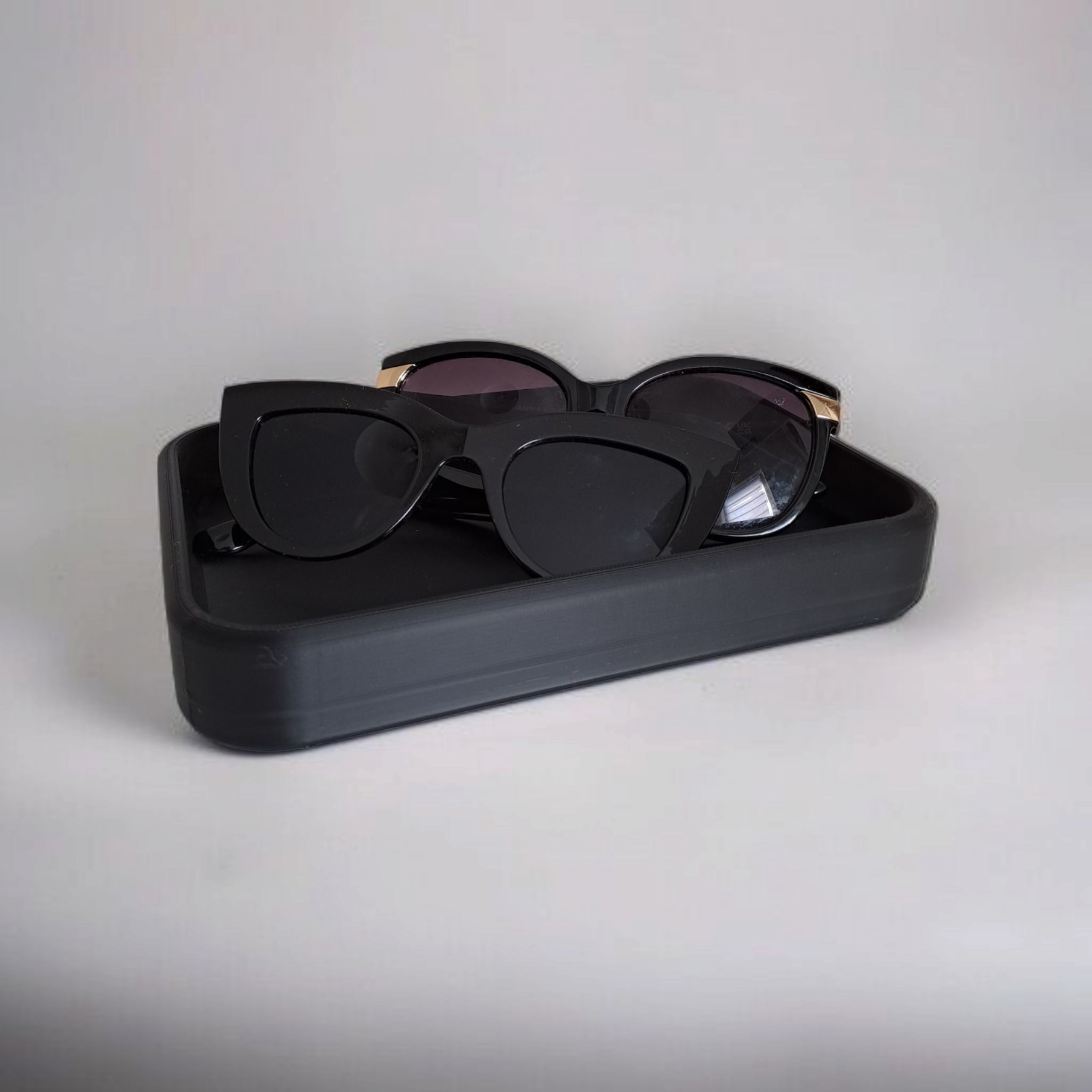 Black sunglasses with gold frames in a black case on a light gray background