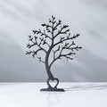 Black tree sculpture with heart at the base on a white background
