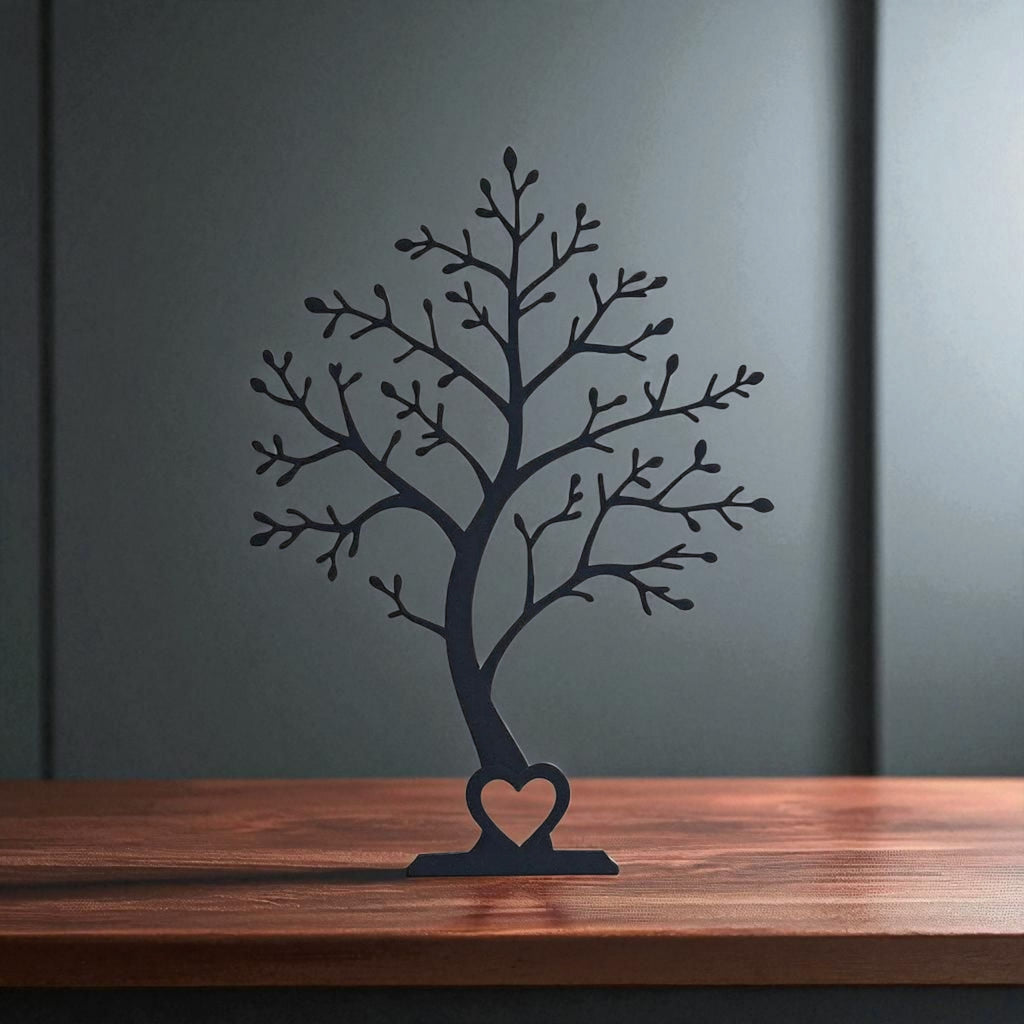Black tree sculpture with a heart at its base on a wooden surface against a dark wall.