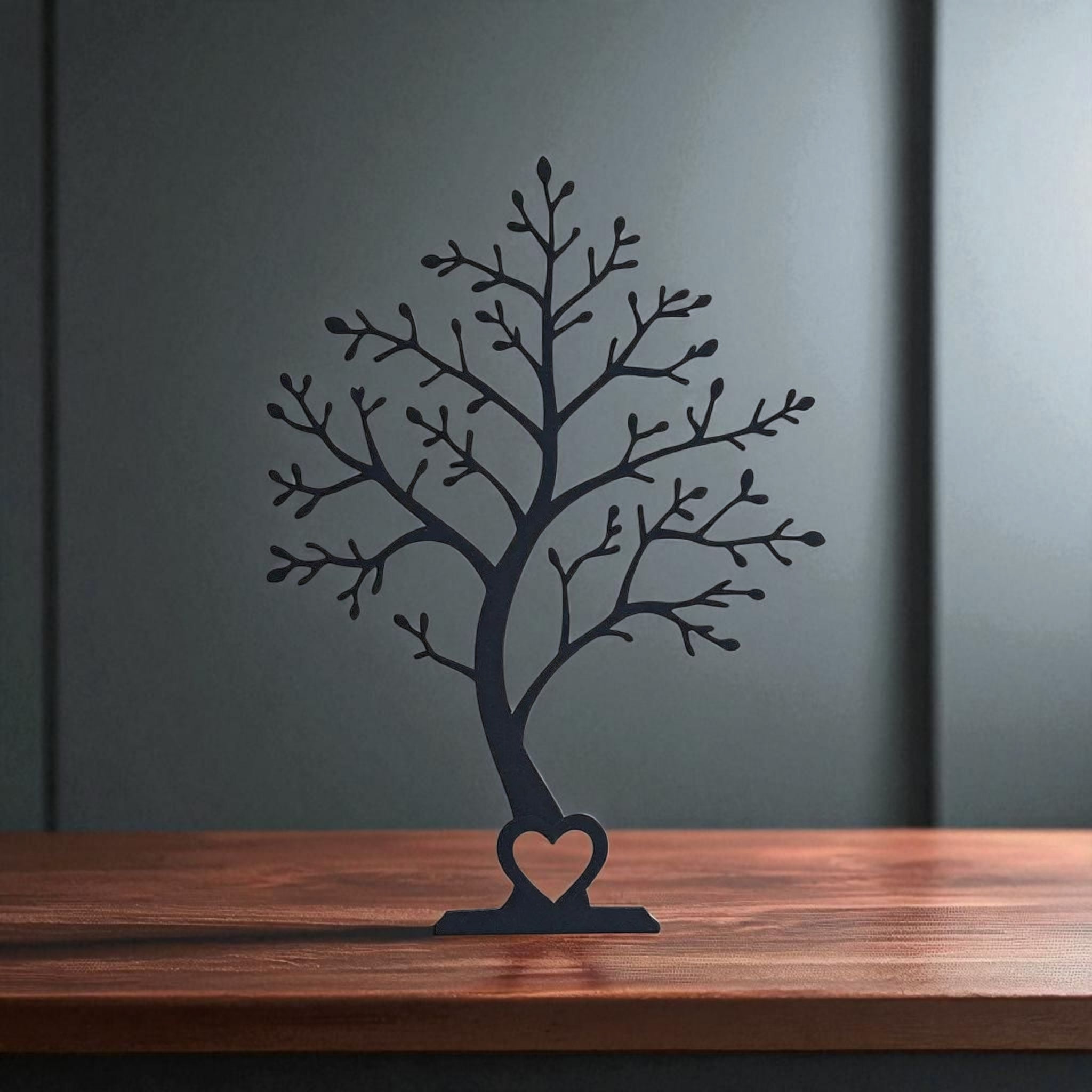 Black tree sculpture with a heart at its base on a wooden surface against a dark wall.