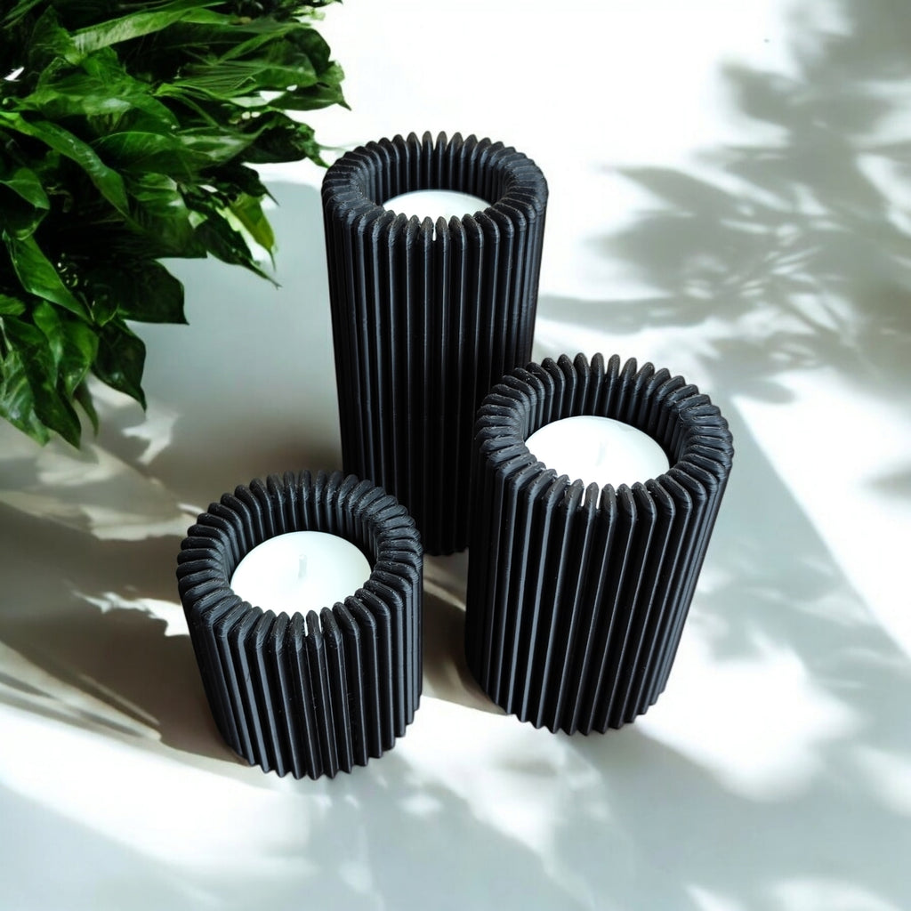 Three black ribbed candle holders on a white surface with a plant in the background
