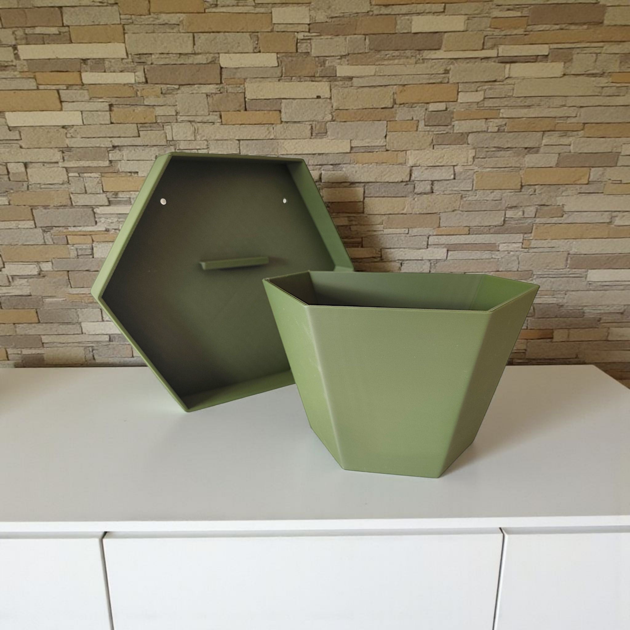 Green hexagonal planter on a white surface with a stone wall background