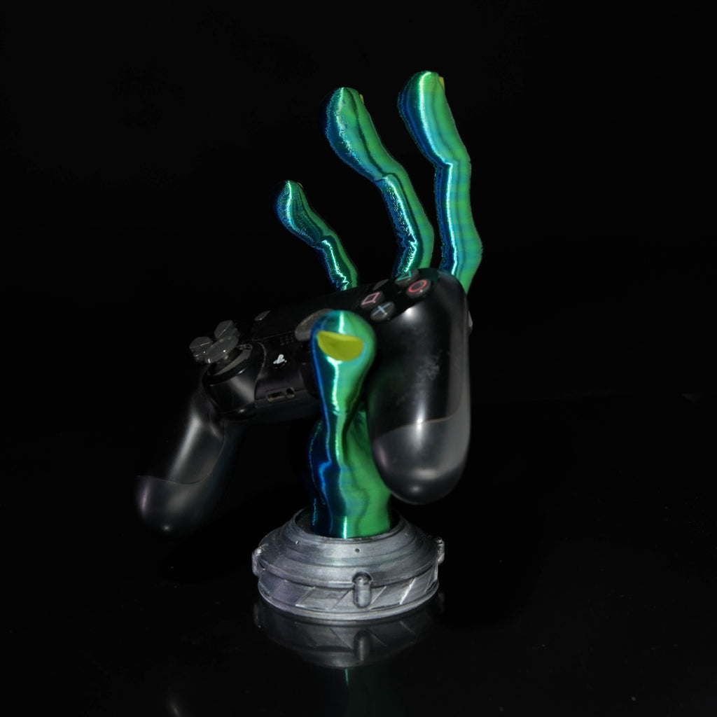4-Finger Alien Hand Controller Holder holding a black gaming controller on a minimalist desk.
