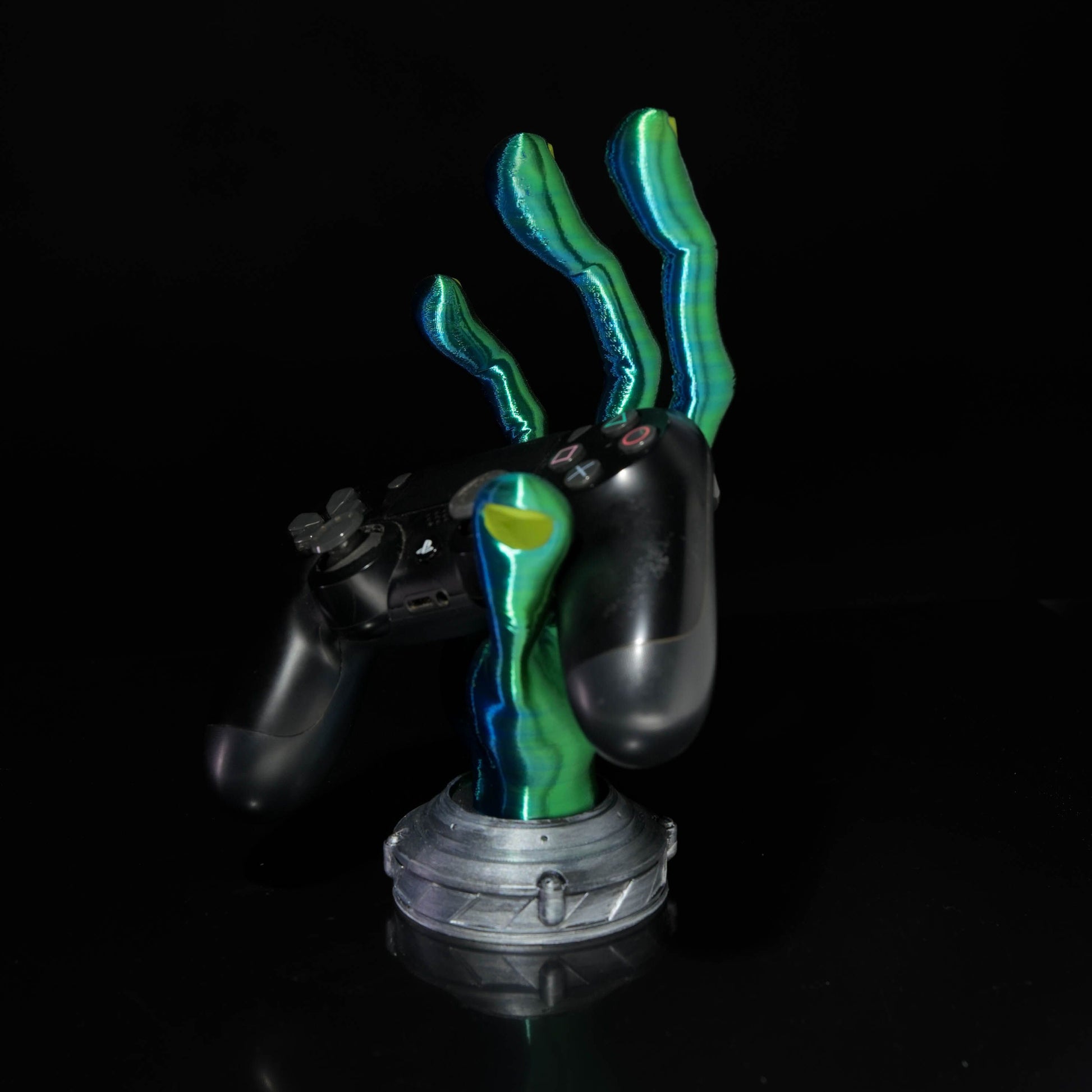 4-Finger Alien Hand Controller Holder holding a black gaming controller on a minimalist desk.