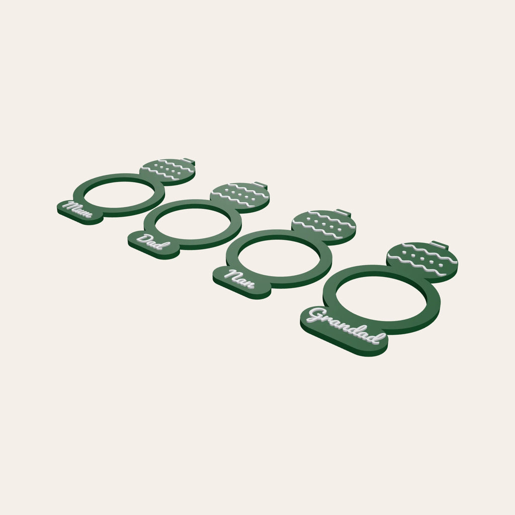 Four green napkin rings with bauble toppers, each with a family name such as Mum or Grandad
