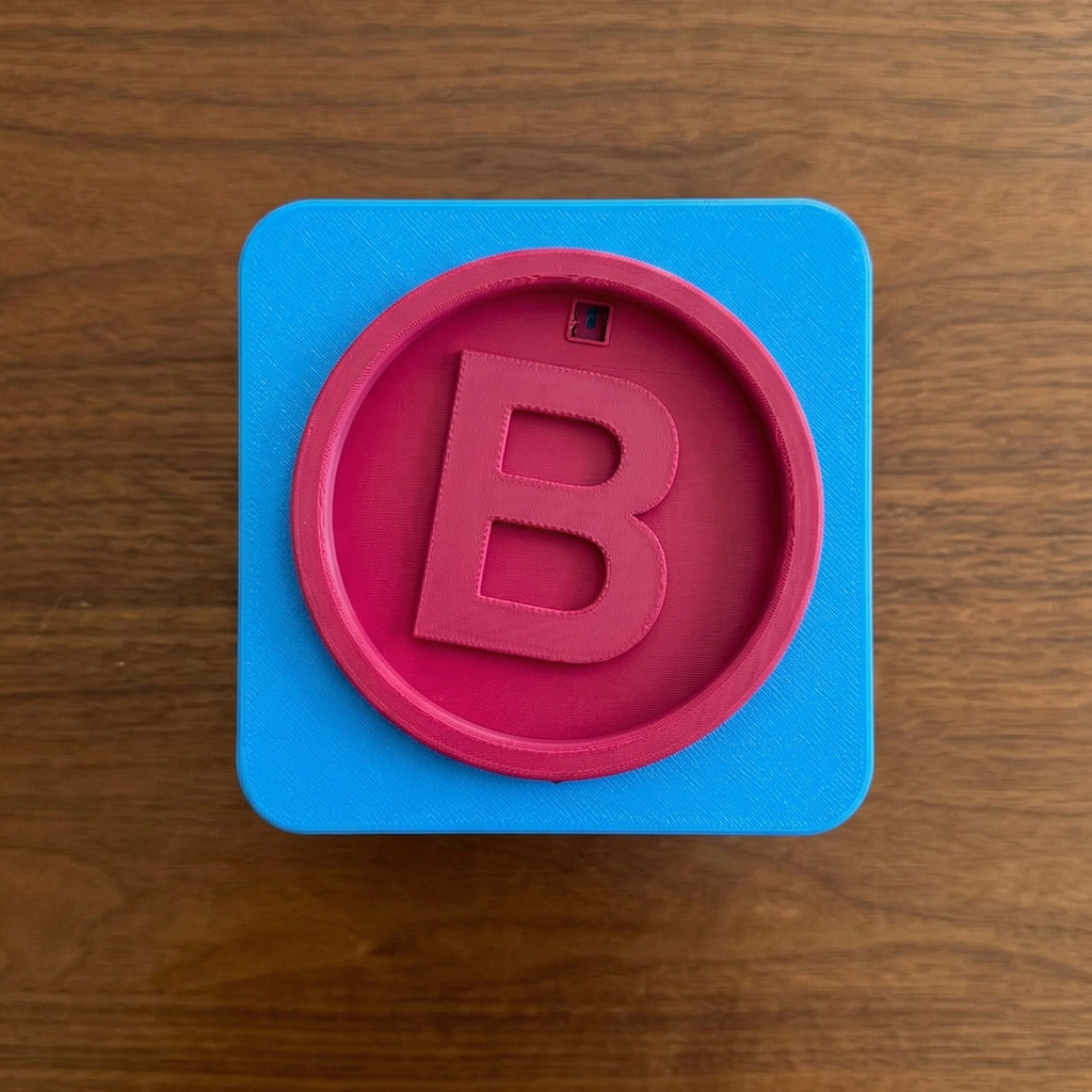 Blue square with a pink circle containing the letter 'B' on a wooden surface