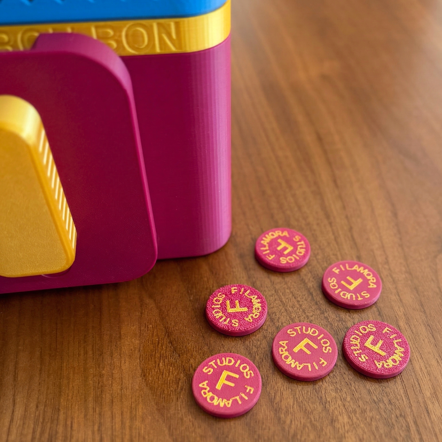 Pink tokens with 'FILMAMORA STUDIOS' text on a wooden surface next to a colorful toy.