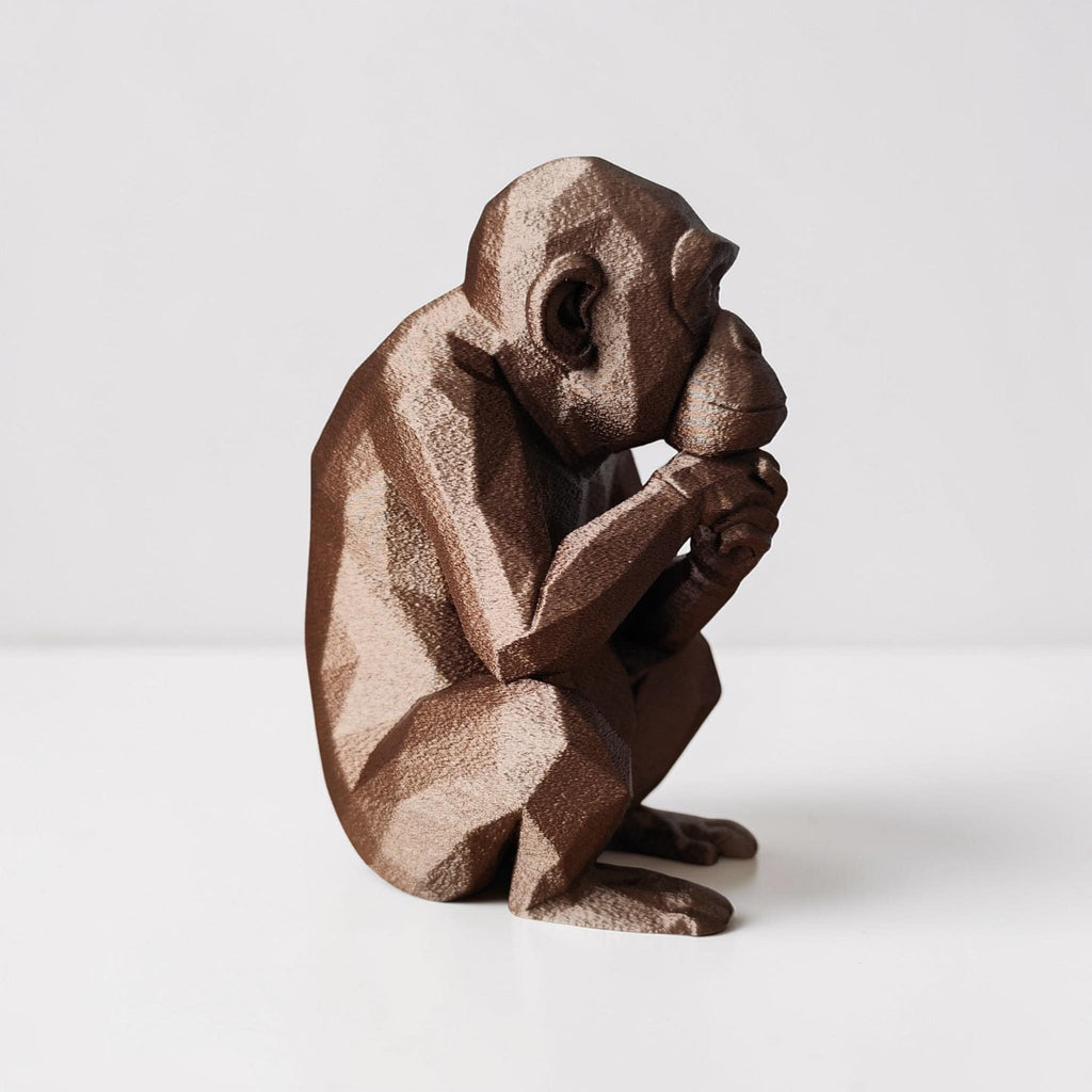Brown monkey figurine sitting with hands on face against a white background
