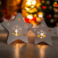 Two star-shaped candle holders with cut-out snowflake designs on a blurred Christmas tree background.