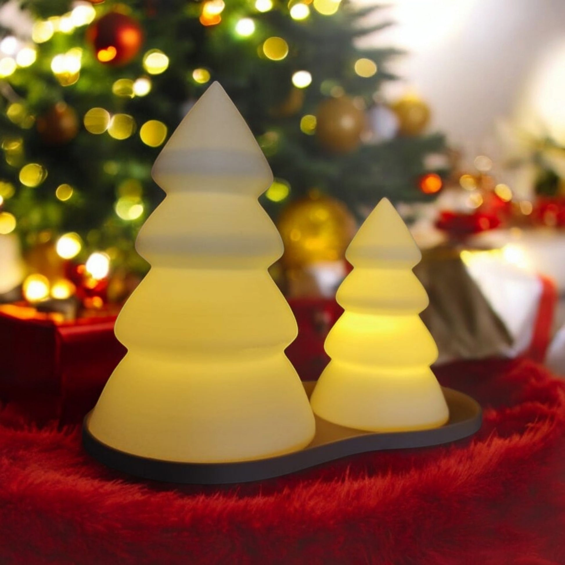 Two Christmas tree-shaped lights on a red surface with a blurred festive background