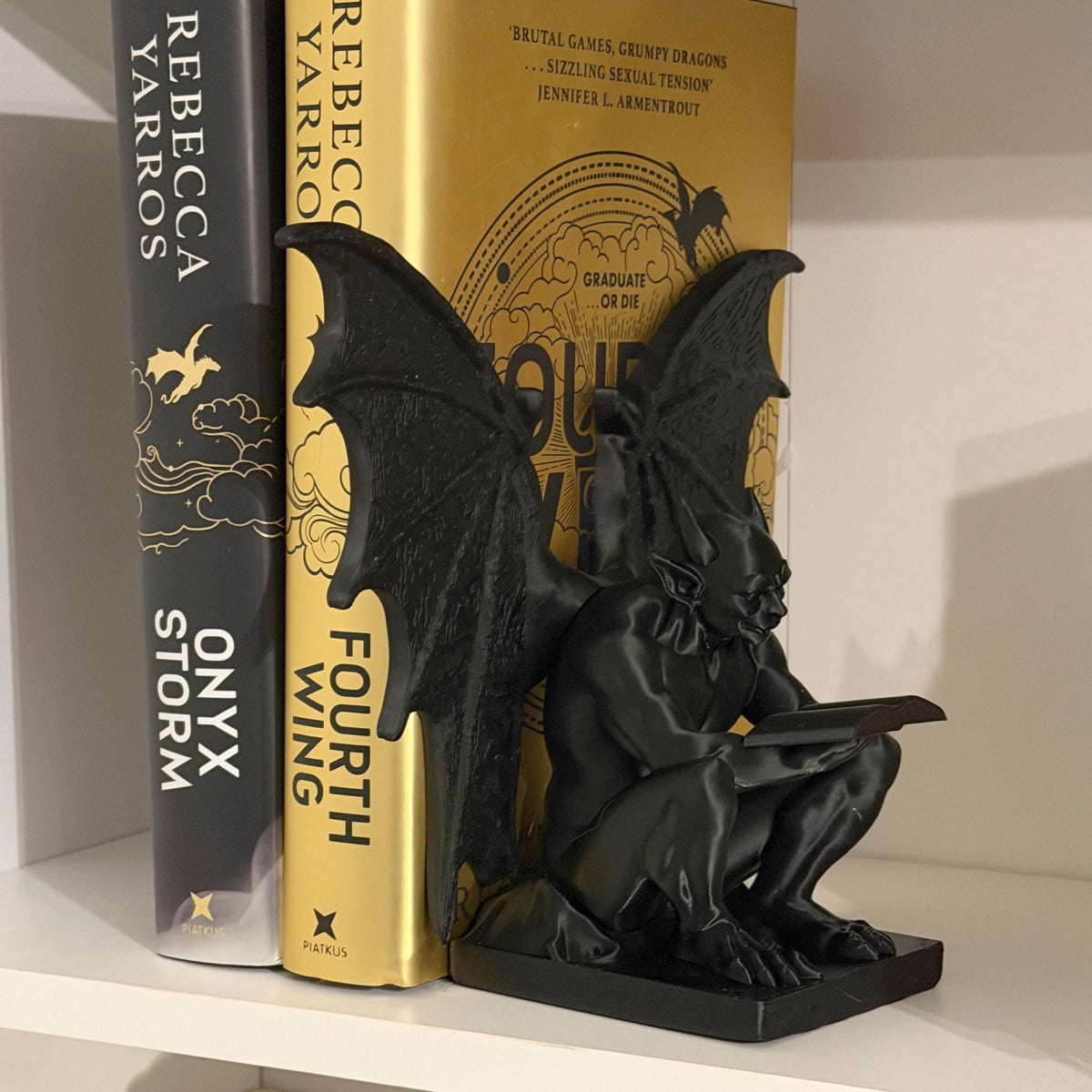 Black gargoyle bookend holding up two hardback books on a white shelf