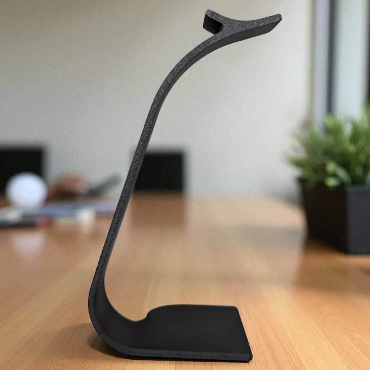 Black headphone stand on a wooden desk with a blurred office background