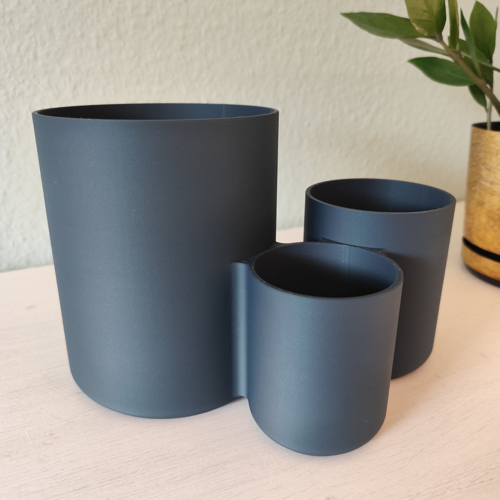 Three blue plant pots of different sizes on a light surface with a textured wall background.