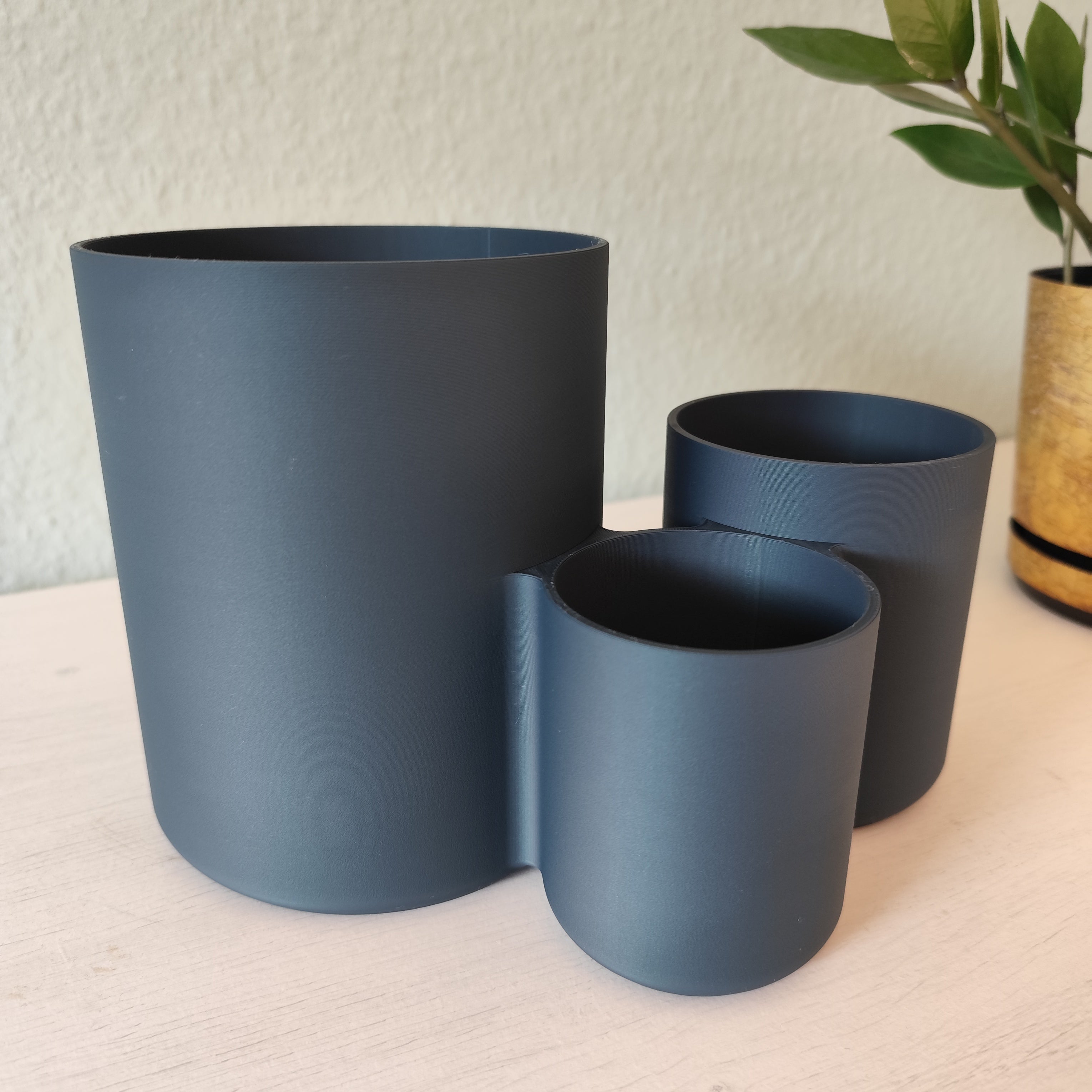 Three blue plant pots of different sizes on a light surface with a textured wall background.