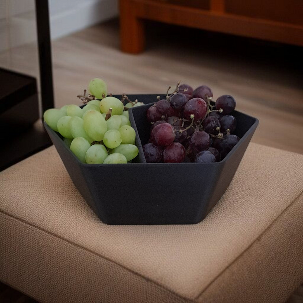 Black bowl with green and red grapes on a beige surface